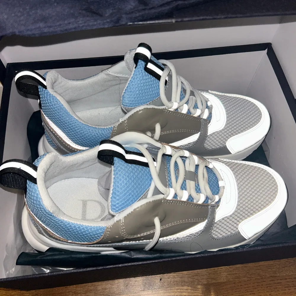 Snygga sneakers från Dior i en kombination av blått, grått och vitt. Skorna har en modern design med snörning och en bekväm sula. Perfekta för en stilren look.. Kengät.