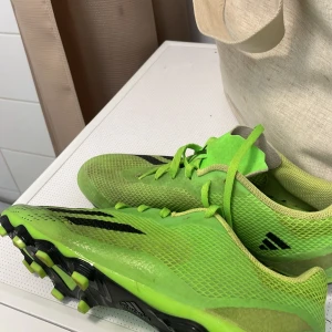 Gröna fotbollsskor från Adidas - Säljer ett par gröna fotbollsskor från Adidas med svarta detaljer. Skorna har snörning och är perfekta för fotbollsplanen. De är tillverkade i syntetmaterial och har en sportig design dock lite fläckar som går bort på en tvätt