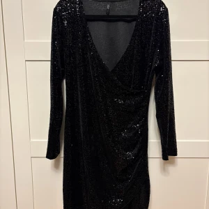 Svart paljettklänning från xlnt  - Snygg svart klänning från Xint med glittrande paljetter och omlott-design. Den har långa ärmar och en v-ringad halslinje, perfekt för en festlig kväll.