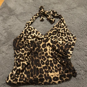 Leopardmönstrad halterneck topp - Snygg leopardmönstrad halterneck topp med knytning i nacken. Perfekt för en djärv look. Toppen har en omlott-design framtill som ger en smickrande passform.