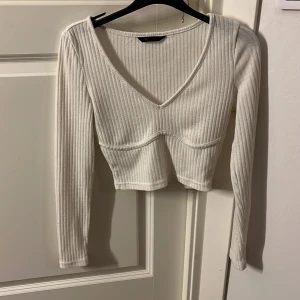Vit ribbad croppad topp - Snygg vit ribbad topp med v-ringning och långa ärmar. Den är croppad. Vill ni se bild på så får ni fråga💕