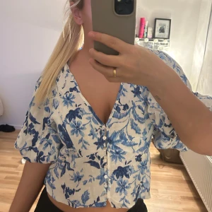 Blommig blus med puffärmar - Säljer en söt blommig blus i vitt och blått med puffiga kortärmar och v-ringning. Perfekt till sommaren!
