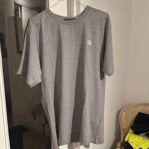 Grå t-shirt från Acne Studios - Snygg grå t-shirt från Acne Studios med en liten logotyp på bröstet. Perfekt för en stilren och avslappnad look. T-shirten har en klassisk passform och är tillverkad i mjukt material för extra komfort.