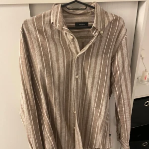 Randig linne skjorta från Matinique  - Snygg beige och vit randig linne skjorta från Matinique. Skjortan har långa ärmar och knappar framtill. Perfekt för en stilren look.