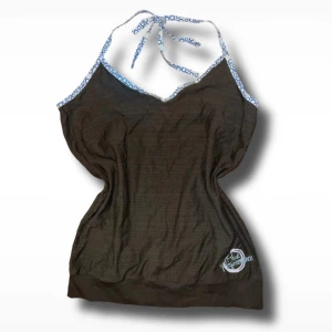 Brun halterneck topp från Peak Performance - 📏: L 40cm / B 27,5cm | Snygg brun halterneck topp från Peak Performance med vita och blå detaljer. Perfekt för en avslappnad stil. Märkeslogga broderad på framsidan.