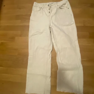 Vita jeansbyxor med knappar - Snygga vita jeansbyxor med knappar framtill. De har en rak passform och är perfekta för en stilren look. Passar bra till både vardag och mer uppklädda tillfällen.