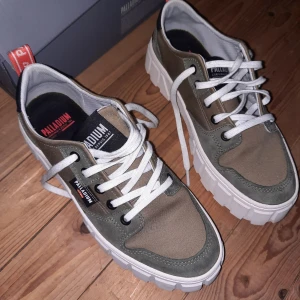 Gröna sneakers från Palladium - Snygga gröna sneakers från Palladium med vit sula och snörning. Skorna har en robust design med detaljer i syntetmaterial och textil. Perfekta för en casual look. Detaljer i mocka, som behöver impregneras. Skorna har använts i ca tio minuter. Något små för mig som har fötter som är ca 24,4 cm, så de borde passa någon vars fötter är 23,5 - 24 cm.
