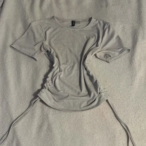 Vit ribbad topp från Divided - Säljer en vit ribbad topp från Divided med korta ärmar och snörning i sidorna för en justerbar passform. Perfekt för en stilren look. 🖤