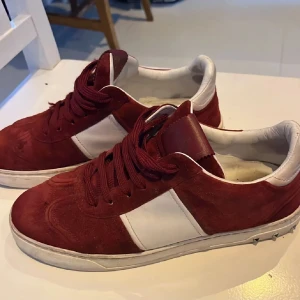 Röda sneakers med vit detalj - Snygga röda sneakers i mocka med vita detaljer på sidan. Skorna har snörning och en bekväm passform. Perfekta för en avslappnad stil.