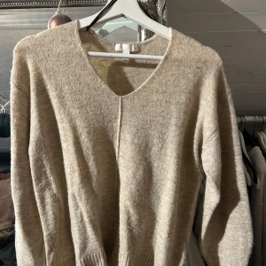 Beige tröja från H&M - Säljer en mysig beige tröja från H&M med v-ringning. Tröjan har långa ärmar och är perfekt för kyligare dagar. Den är enkel och stilren, vilket gör den lätt att matcha med olika outfits.