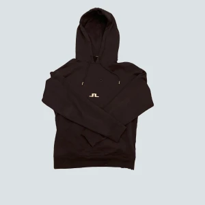 Mörkblå hoodie från J.Lindeberg - Säljer en stilren mörk hoodie från J.Lindeberg med en diskret logga på bröstet. Tröjan har en klassisk design med huva och dragsko, perfekt för en avslappnad look. Passar bra till både jeans och träningsbyxor.