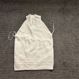 Vit ärmlös topp - Säljer en stickad topp som är perfekt till sommaren. Skön och sitter perfekt vid midjan. Säljer då den blivit lite liten och inte kommer till så mycket användning