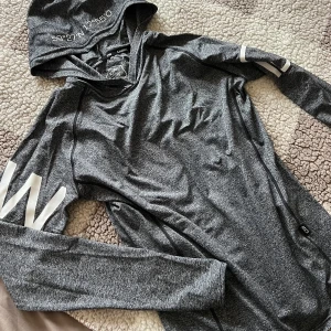 Grå hoodie från ICANIWILL, storlek M - Snygg och modern tränings huvtröja från Icaniwill i gråmelerad färg. Tröjan har en huva med detaljerad text, samt tryck på ärmarna och ryggen. Sparsamt använd och i mycket gott skick