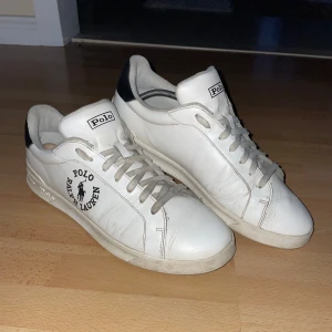 Vita sneakers från Polo Ralph Lauren - Snygga vita sneakers från Polo Ralph Lauren med svart logga på sidan och hälen. Skorna har snörning och en klassisk design som passar perfekt till vardags. Tillverkade i skinn med en bekväm sula. Knappt använda!😀