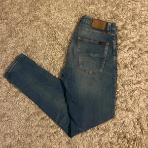 Blå jeans från Nudie Jeans - Snygga blå jeans från Nudie Jeans med klassisk femficksdesign. De har en straight slim passform och är tillverkade i orgsnisk bomull. Perfekta för en avslappnad stil. Strlk 31/30, fraktar antingen samma dag slm köp eller dagen där på. Sänker priset 50kr vid snabb och smidig affär💯