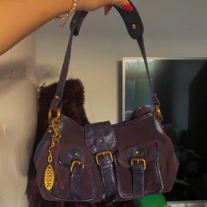 Cool väska💓 - Snygg lila axelväska från Ri2K med dekorativa spännen och gulddetaljer. Väskan har en praktisk axelrem och flera fickor framtill. Perfekt för att ge din outfit en cool touch.💓❤️