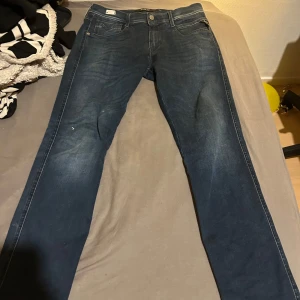 Blå jeans från Replay - Snygga blå jeans från Replay i modellen Anbass. De har en klassisk femficksdesign och en knappgylf. Perfekta för en stilren look.