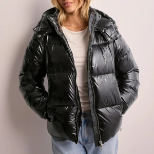 Svart glansig pufferjacka - Snygg svart glansig pufferjacka med dragkedja och huva från Nelly. Använt 1 gång köpt för 799kr