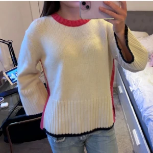 Stickad tröja!!! - Säljer en vit stickad tröja med röda och svarta detaljer. Tröjan har långa ärmar och en ribbad kant vid ärmslut och nederkant. Knappt använd! Så snygg❣️