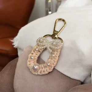Nyckelring med pärlor och rosett - Elegant nyckelring med en dekorativ rosett och pärlor. Den har en guldig karbinhake för enkel fastsättning. Perfekt som en stilfull accessoar till väskan eller nycklarna.