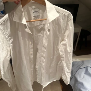 Vit skjorta från Oscar of Sweden - Snygg vit skjorta från Oscar of Sweden i slim fit. Skjortan har långa ärmar och knappar framtill. Perfekt för en stilren look. Materialet är non iron vilket gör den lättskött och bekväm.