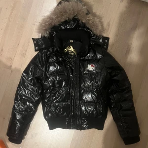 Svart pufferjacka från Victoria Couture x hello kitty - Säljer en svart glansig pufferjacka från en gammal kollektion av Victoria Couture x Hello Kitty från 2008. Jag vill vara tydlig med att detta är en jacka som hängt med i många år och är väldigt välanvänd, därav tillkommer defekter på yttersidan av tyget. Det är inget som syns om man inte letar, bilder kan skickas. 🥰80% dun fodring och äkta päls på kragen, därav att den hållt sig så fin genom alla år. Detta är en jacka som kommer hålla länge till!