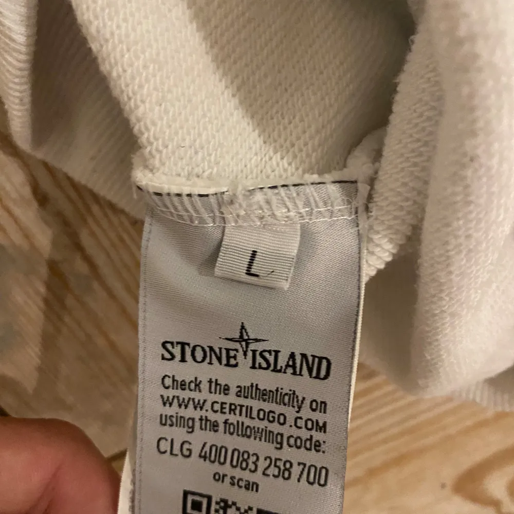 Säljer en stilren vit tröja från Stone Island. Den är långärmad och har en klassisk passform. Perfekt för både vardag och lite mer avslappnade tillfällen. Tröjan är äkta det finns qr-kod, inga skador och tröja passar som en storlek M.. Tröjor & Koftor.