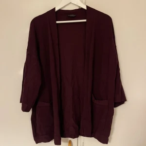 Vinröd kofta - Säljer en mysig vinröd kofta med en avslappnad passform. Den har långa ärmar och två praktiska fickor framtill. Perfekt för höst och vinter när du vill hålla dig varm och bekväm. Passar till både vardag och mysiga hemmakvällar.