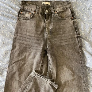 Gråa jeans - Jeans från Ginatricot i storlek 32, knappt använda, fint skick och inga defekter. Hög/mid midja och rak modell. Dekorativa slitningar vid anklarna och runt fickor.