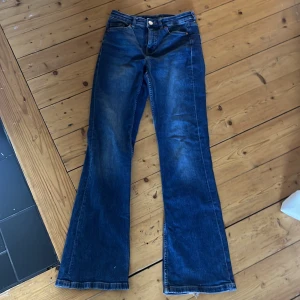 Blå bootcut jeans - Säljer ett par snygga blå bootcut jeans i storlek 36. De har en klassisk femficksdesign och är gjorda i denim. Perfekta för en avslappnad look! Det finns en liten slits vid fållen som ger dem en cool, avslappnad stil.