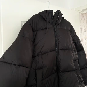 Svart pufferjacka från H&M - Säljer en svart pufferjacka (dunjacka) från H&M i storlek S. Den är perfekt för kalla vinterdagar med sin tjocka vaddering och huva. Jackan har en dragkedja framtill och är riktigt skön och varm. Passar både till vardags och när du vill hålla stilen i kylan.