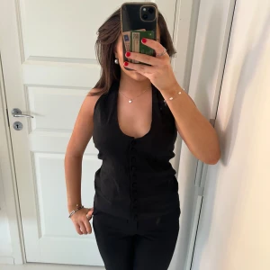 Svart ärmlös topp med knappar - Säljer en as snygg svart topp med knappar framtill. Toppen har en djup urringning och en tight passform. Den är öppen i ryggen. Toppen har prislappen kvar och är helt ny och köptes för 359kr🤗💖