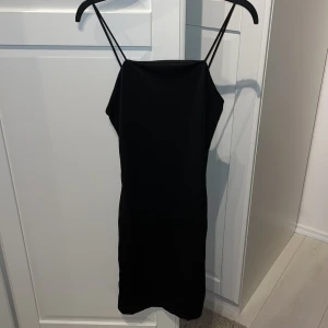 Svart klänning från BikBok - Säljer en stilren svart klänning från BikBok i storlek XS. Klänningen är ärmlös med smala axelband och har en tight passform som passar perfekt för festliga tillfällen. Materialet känns mjukt och bekvämt mot huden.