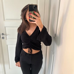 Svart croppad topp med knytning - Säljer en snygg svart croppad topp med v-ringning och långa ärmar. Den går att ändra som man vill med hjälp av att dra i banden beroende på hur kort man vill att toppen ska vara🤗 Den passar perfekt till fest men även till middagar💖 kontakta mig om du har några frågor. Pris går att diskutera!