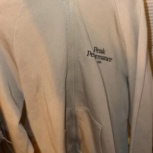 Beige hoodie från Peak Performance - Säljer en snygg beige hoodie från Peak Performance i storlek XL. Den har en dragkedja framtill och en mysig huva. Perfekt för både höst och vår, och den är superbekväm att ha på sig. Passar perfekt för chill dagar eller när du vill ha en avslappnad stil.