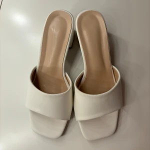 Vita klackskor med öppen tå - Säljer ett par stilrena vita klackskor med öppen tå. De har en bred rem över foten och en bekväm blockklack. Perfekta för sommarens fester eller en elegant vardagslook. Har en smutsfläck på klacken som jag inte testat få bort.