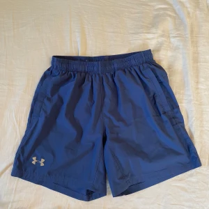 Blå träningsshorts från Under Armour -  Korta Under Armour-shorts perfekta för träning eller löpning. Shortsen har fickor på sidorna och är i relativt fint skick. Tveka inte att höra av dig om du har frågor eller vill ha fler bilder!