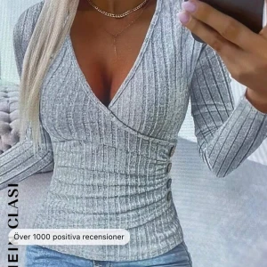 Grå ribbad omlottopp - Säljer en snygg grå ribbad omlottopp med v-ringning. Den har långa ärmar och en tight passform. 