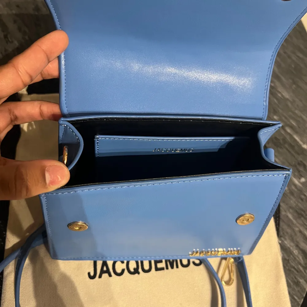 Säljer en superfin blå handväska från Jacquemus. Den är i skinn och har en stilren design med ett elegant handtag och en avtagbar axelrem.  Magnetisk stängning. Har inte kvitto tyvärr,  Den kommer med en dustbag. 20 cm bred, 15 cm lång utan handtaget. Väskor.