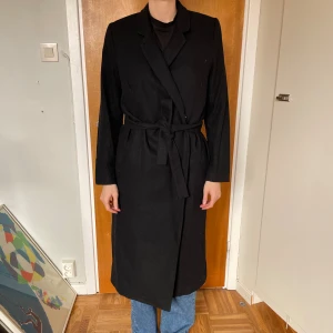 Svart kappa  - Svart kappa från Weekday. Strlk M. Gott och använd skick. 55% ull i ytterfoder och 100% polyester innerfoder.