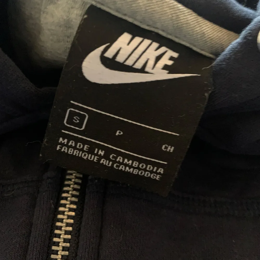 Säljer en mörkblå hoodie från Nike i storlek S. Den har en dragkedja framtill och en klassisk Nike-logga på bröstet. Perfekt för höst och vinter, och den är superbekväm med en skön passform. Huvan har snören för justering. Perfekt för både träning och vardag!. Tröjor & Koftor.