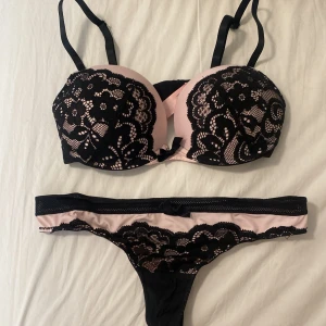 Svart och rosa spets-bh - Säljer en superfin bh i svart och rosa med spetsdetaljer. Den har justerbara axelband och en liten rosett framtill. Perfekt för att känna sig extra fin till vardags eller speciella tillfällen. Passar bra under en klänning eller topp med djup urringning.