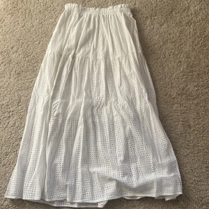 Vit långkjol med broderad design - Säljer en superfin vit långkjol med broderad design, perfekt för sommarens varma dagar. elastiska midjan gör att den också kan användas som en klänning!!. Perfekt för en avslappnad dag på stan eller en somrig fest! 🌼