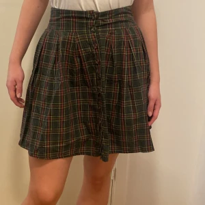 Rutig kjol från Bondelid - Säljer en superfin rutig kjol från Bondelid i storlek S. Kjolen har en klassisk grön bas med röda och gula rutor, perfekt för höst och vår. Den har knappar framtill och en bekväm passform som sitter snyggt i midjan. Perfekt för både vardag och fest! 🍂