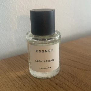 Lady Essnce Eau de Parfum - Säljer en elegant och stilren parfymflaska från Essnce med doften Lady Essnce. Flaskan är genomskinlig med en enkel vit etikett och har ett svart lock. Perfekt för den som vill ha en klassisk och tidlös doft på hyllan. Passar både till vardags och fest!