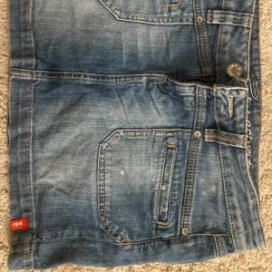 Blå jeanskjol från ACG - Säljer en snygg blå jeanskjol från ACG. Kjolen har en klassisk femficksdesign med dragkedja och knapp framtill. Perfekt för en avslappnad vardagslook eller en somrig utflykt. Passar bra med en t-shirt eller en stickad tröja för kyligare dagar.