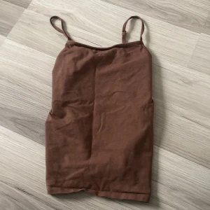 Brun linnetopp från Lindex - Säljer en enkel och stilren brun linnetopp från Lindex i storlek 146/152. Perfekt för varma sommardagar eller som ett basplagg under en kofta. Toppen har smala axelband och är i ett mjukt material.