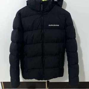 Calvin Klein jacka  - En fin svart Calvin Klein jacka använd 1 år, den allt är i bra skick förutom att märket på sidan är slitet av lite, det är bara att sy så är den som ny, pris kan diskuteras vid snäbbäffar. 