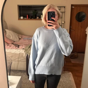 Ljusblå stickad tröja - Säljer en supermysig ljusblå stickad tröja som är helt oanvänd. Den har en avslappnad passform med långa ärmar och ribbade kanter vid ärmslut och nederkant. 