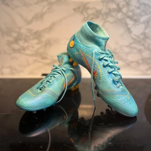 Turkosa fotbollsskor från Nike - Säljer ett par snygga turkosa fotbollsskor från Nike i mycket bra skick. Skorna har en cool design med orange detaljer och snörning. Perfekta för fotbollsträning och matcher. Sulan har flera dobbar för bra grepp på planen. Passar dig som vill sticka ut på planen! (Priset kan diskuteras!)